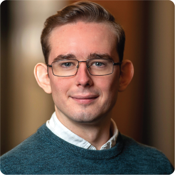 A color photo of a man with glasses smiling for a photo.