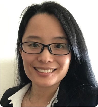 A color photo of a woman with glasses, smiling for a picture.