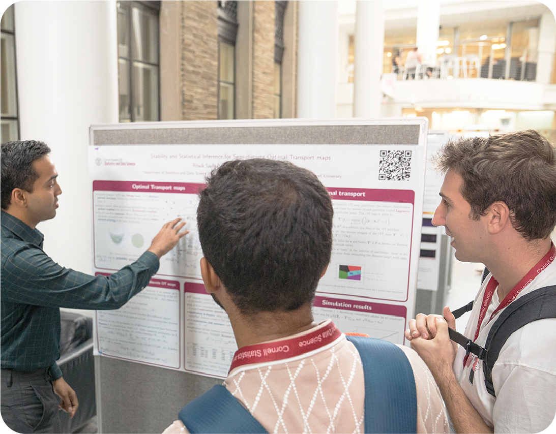 A color photo showing a person explaining his research poster to a couple of fellow students.