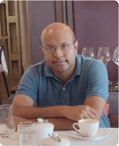 A color photo of a man sitting at a table in a restaurant.