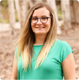 A color photo of a woman smiling for a photo outdoors. 