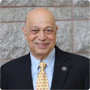 A color photo of a man wearing a suit and tie in front of a wall