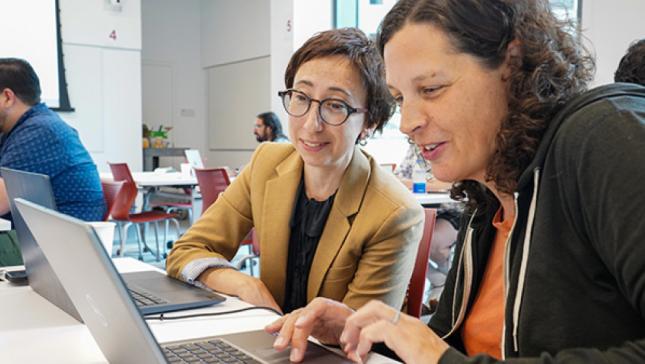 Two woman with brown hair look at a laptop screen