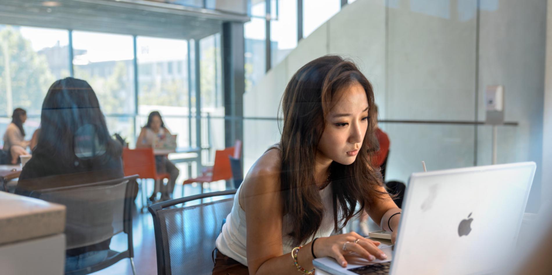 A color photo of a woman working at a laptop in Gates Hall.