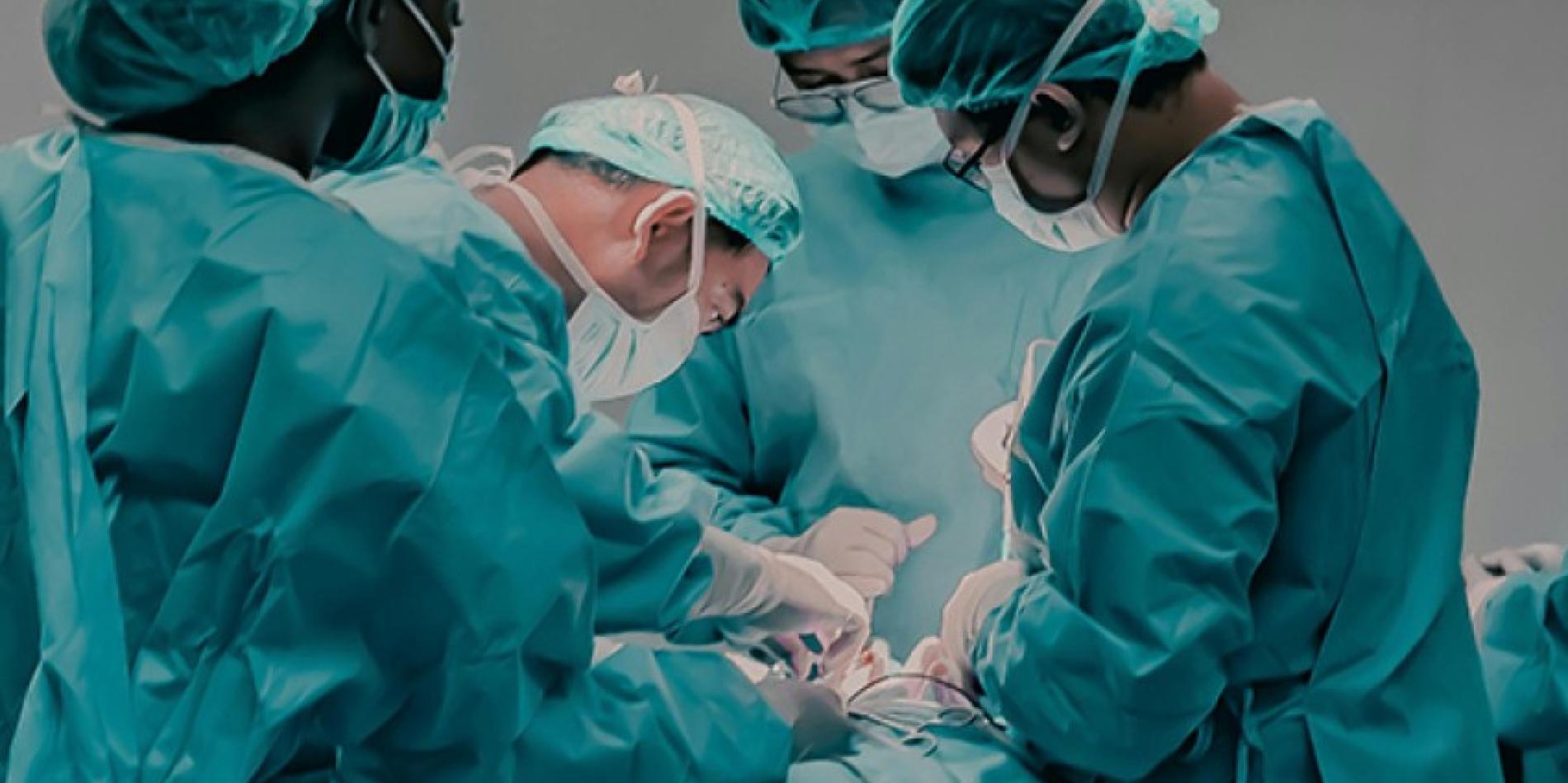 Four healthcare professionals in green gowns perform surgery on a patient.