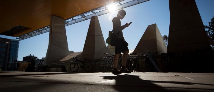Person walking under Gates Hall overhang, sun setting behind them