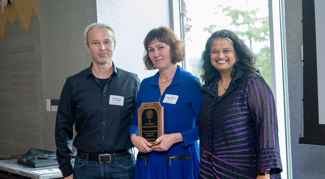 A color photo showing a man and two women posing for a photo. The woman in the middle is holding an award