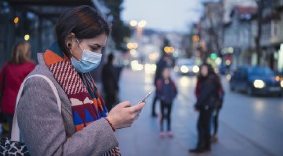 A woman, wearing a medical mask, looks at her smartphone.