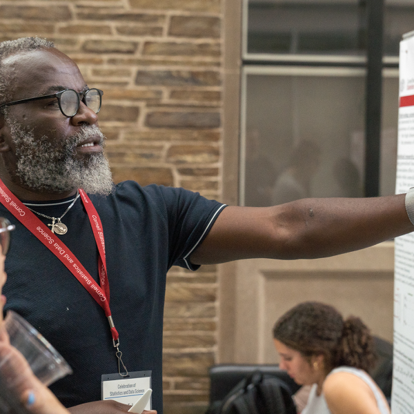 A color photo of a man pointing at a poster while discussing it with a young woman.
