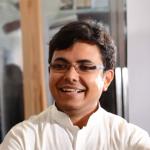 A photo of Karthik Sridharan, a smiling man with short dark hair, glasses and a white shirt