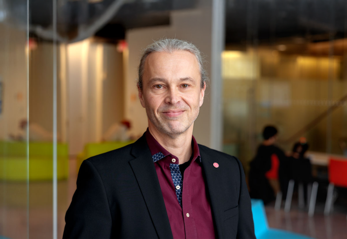 A portrait of Thorsten Joachims, a man with gray hair and a dark red shirt smiling at the camera