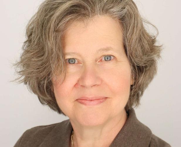 a women with gray-brown short hair smiles wearing a brown collared shirt