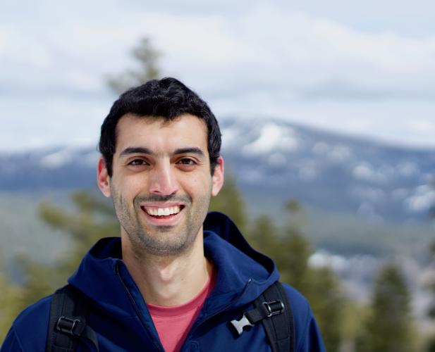 color portrait of man with dark hair on mountain, smiling