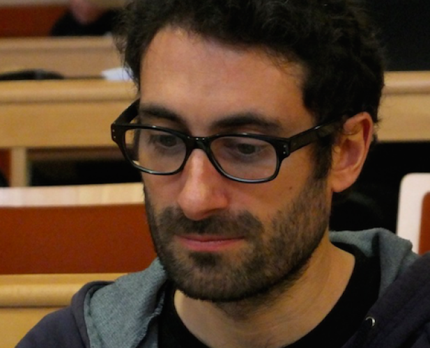 man with glasses, short dark hair and beard looking down