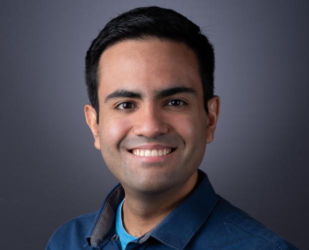 A photo of Christopher De Sa, a smiling man with short dark hair and a blue shirt.