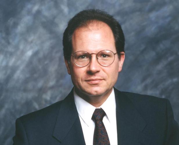 color portrait of man in suit, dark short hair, wire framed glasses