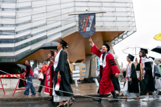 A color photo showing people walking to Cornell University graduation behind the Cornell Bowers flag