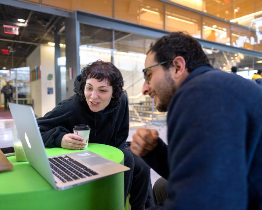  woman and man, both with dark hair, work on a laptop in Gates lobby