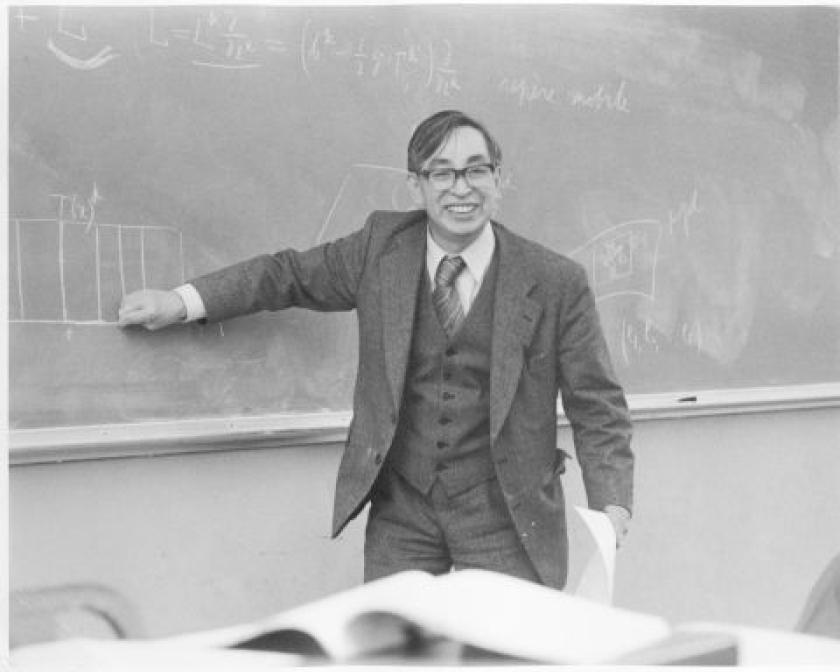 Black and white photo of man in suit pointing to chalkboard