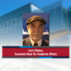 A color photo of a man wearing a hat smiling for a photo in front of a blurred image of Gates Hall in Ithaca, NY