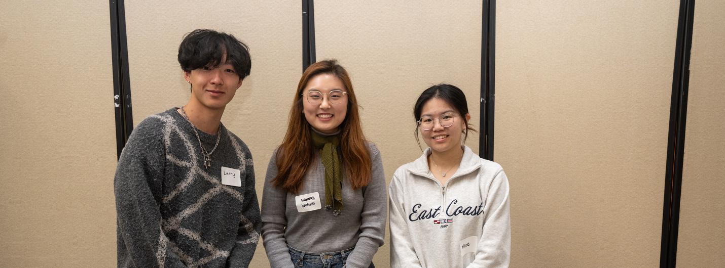 three students standing behind a table at BOOM 2025, laptops open on table