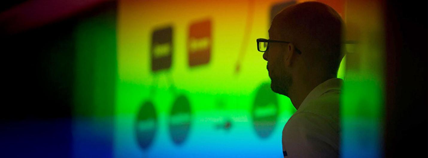 Faculty member observes a multicolored presentation on screen.